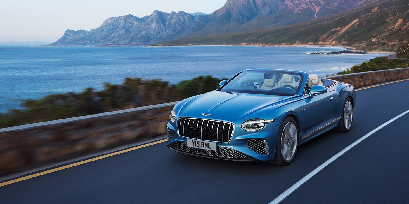 Exclusive Cars Vertriebs GmbH New Bentley Continental GTC Azure convertible in Light Windsor blue paint with 22 inch Azure wheels and chrome grill, driving dynamically by the sea