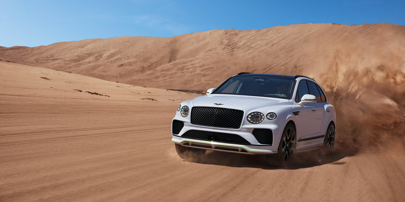 Exclusive Cars Vertriebs GmbH Bentley Bentayga Speed SUV front three quarter in Snow Quarts Pearlescent by Mulliner white paint driving dynamically through the desert