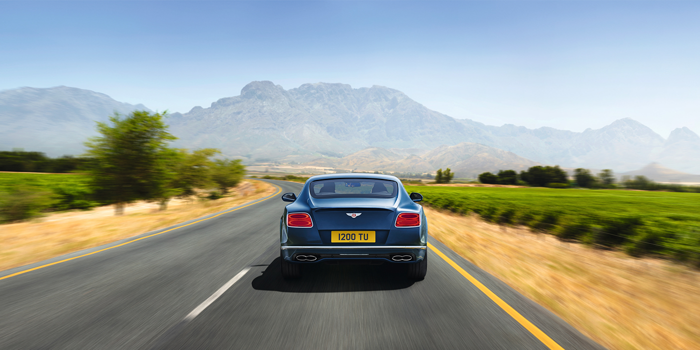 Exclusive Cars Vertriebs GmbH Bentley Pre Owned Bentley Continental GT in Marlin blue paint seen from rear on country road