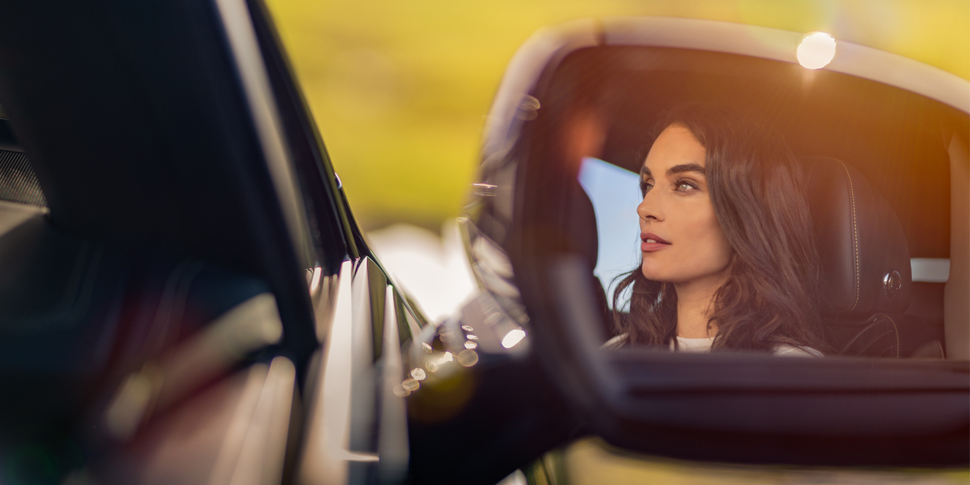 Exclusive Cars Vertriebs GmbH profile of dark haired woman's face in mirror of Bentley car in sunlight