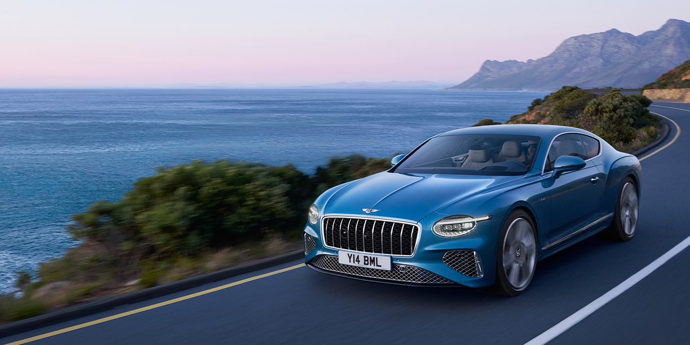 Exclusive Cars Vertriebs GmbH New Bentley Continental GT Azure coupe in Light Windsor blue paint with 22 inch Azure wheels and chrome grill, driving dynamically by the sea