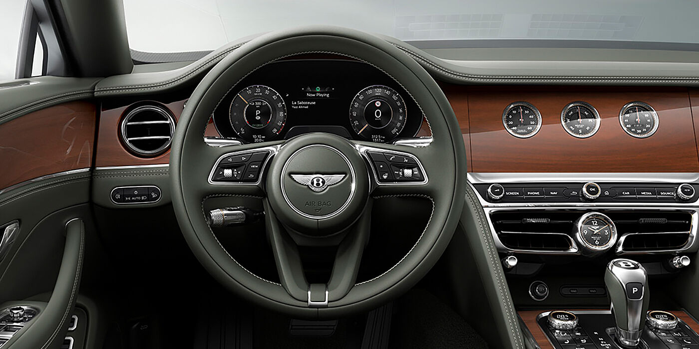 Exclusive Cars Vertriebs GmbH New Bentley Flying Spur sedan front cabin in Cumbrian Green hide and Crown Cut walnut veneer showing steering wheel and Rotating Display with three clocks on face