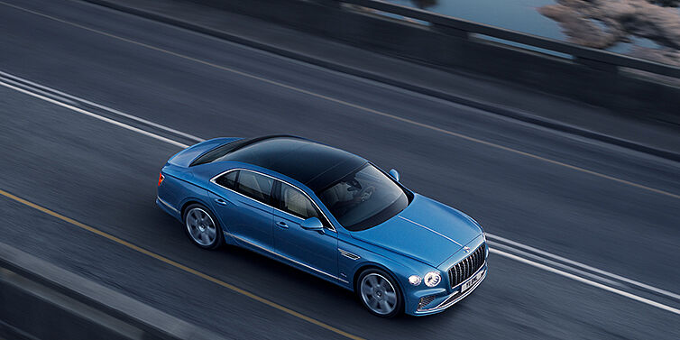 Exclusive Cars Vertriebs GmbH New Bentley Flying Spur Azure sedan in Light windsor blue paint by Mulliner, with 22 inch Azure wheels seen from overhead driving dynamically on a country road