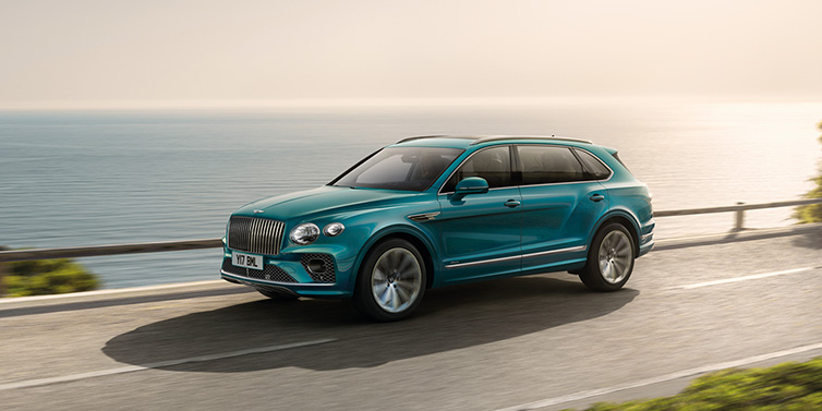 Exclusive Cars Vertriebs GmbH Bentley Bentayga Extended Wheelbase Azure SUV in Topaz blue paint driving dynamically by the ocean