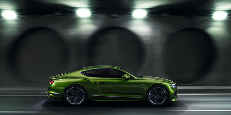 Exclusive Cars Vertriebs GmbH Bentley Continental GT Speed coupe profile in Tourmaline Green driving dynamically past a concrete wall at night