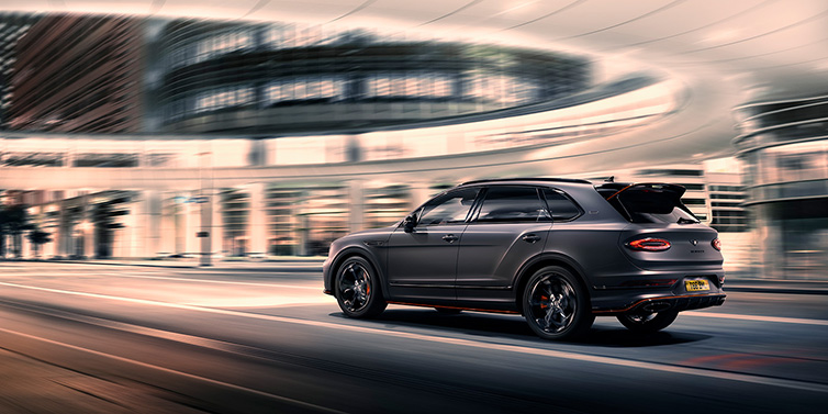 Exclusive Cars Vertriebs GmbH Bentley Bentayga S Black Edition SUV rear three quarter in Anthracite Satin paint driving dynamically through a city at night