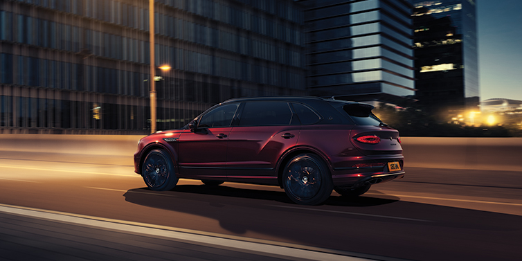 Exclusive Cars Vertriebs GmbH Bentley Bentayga Extended Wheelbase Mulliner SUV in Cricket Ball red paint driving dynamically in city at night