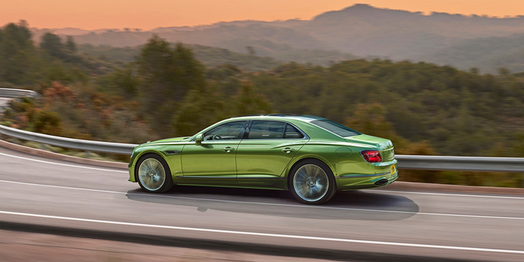 Exclusive Cars Vertriebs GmbH Bentley Flying Spur Speed sedan side profile in Tourmaline Green paint driving dynamically on a mountain road at sunset