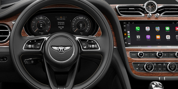 Exclusive Cars Vertriebs GmbH Bentley Bentayga SUV front interior detail of steering wheel and driver screens surrounded by Beluga black hide and Crown Cut Walnut veneer